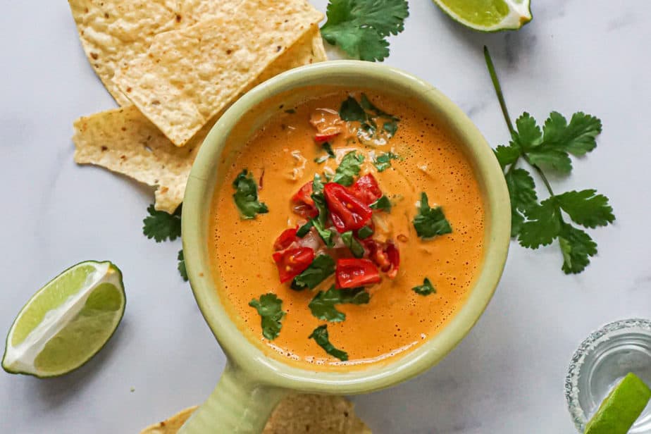 creamy vegan cashew queso in a bowl with tomatoes, cilantro, and chips.