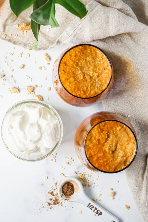 pumpkin pie overnight oats in a orange glass jar with whipped cream, pumpkin pie spice, and crushed graham crackers 